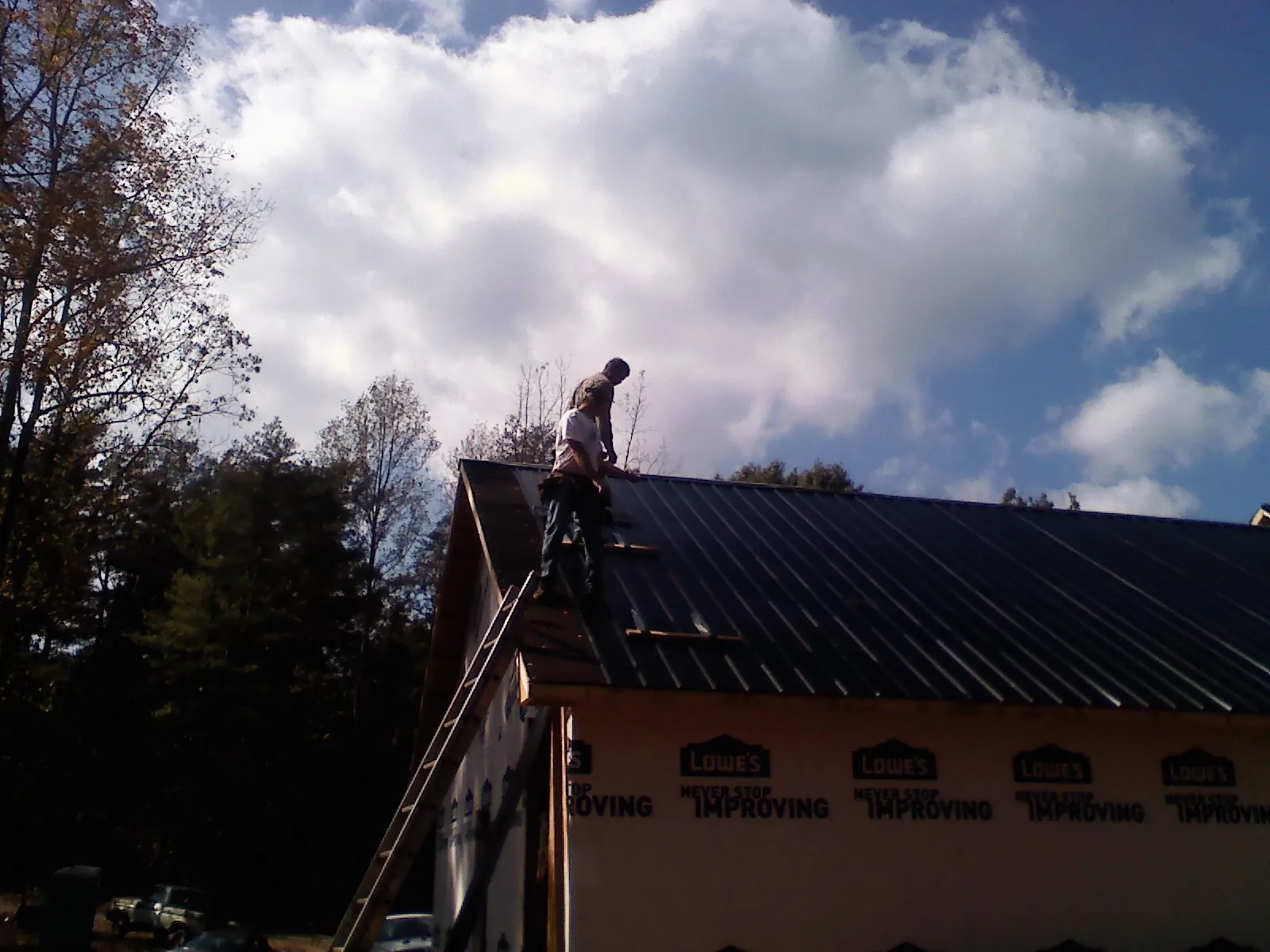 Roofer fastening dark metal panels high against a cloudy sky, from a Roof Inspection job in Blairsville
